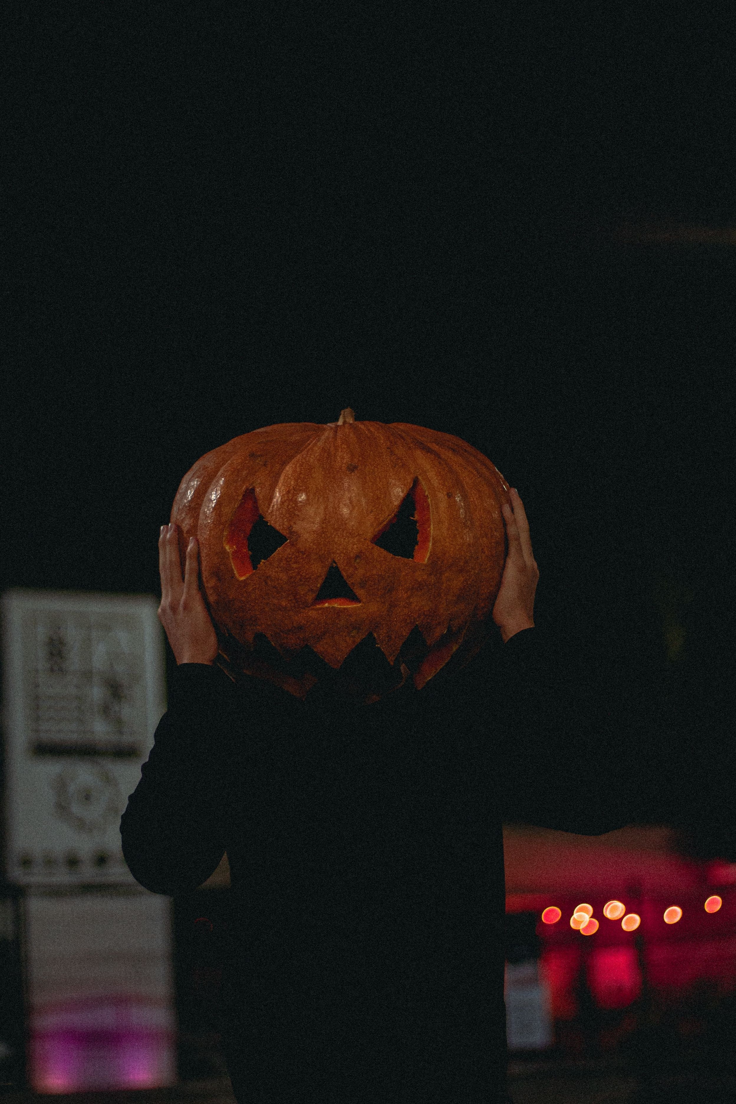 Person in an eerie jack-o-lantern mask against a black background, horror convention style